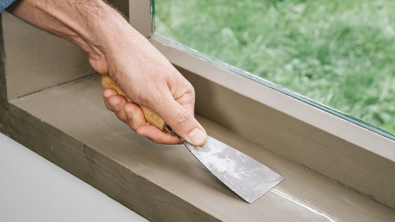 Ein mit Spachtelmasse gefüllter Riss in einem Fensterbrett wird mit einem Spachtel geglättet