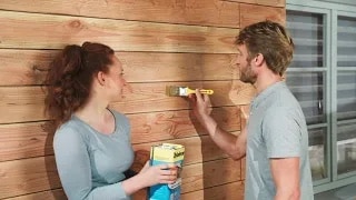 Ein Mann und eine Frau streichen eine Fassade mit der Holzschutz-Lasur Plus von Xyladecor.