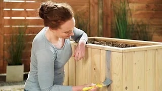 Eine Frau streicht ein Hochbeet mit der Holzschutz-Lasur Plus von Xyladecor.