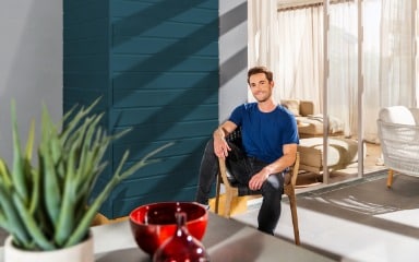 Mann sitzt auf einer Terrasse vor einer in Nachtblaue gestrichenen Fassade 