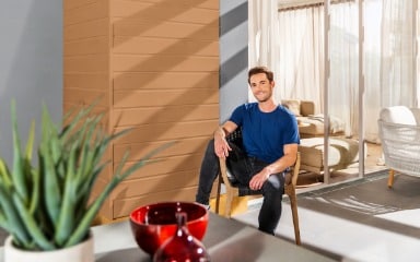 Mann sitzt auf einer Terrasse vor einer in Sandgelb gestrichenen Fassade