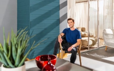 Mann sitzt auf einer Terrasse vor einer in Sommerblau gestrichenen Fassade