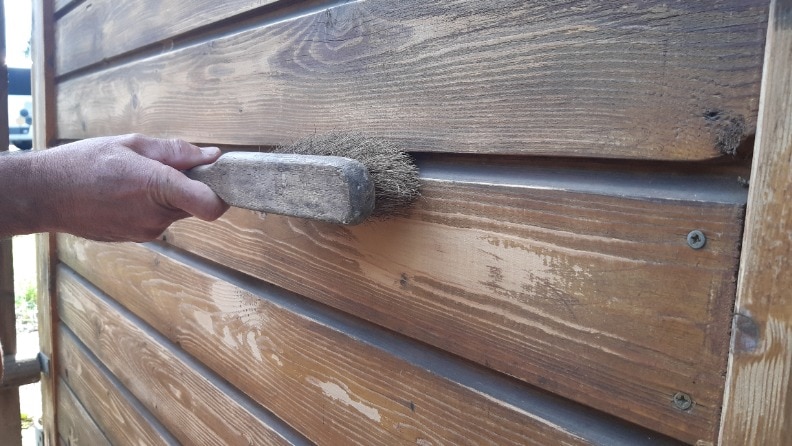 Ein Mann bürstet vor dem Streichen seinen Carport mit einem Handfeger ab