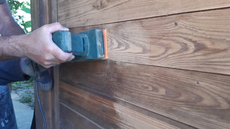 Ein Mann schleift vor dem Streichen seinen Carport mit einem Schwingschleifer an