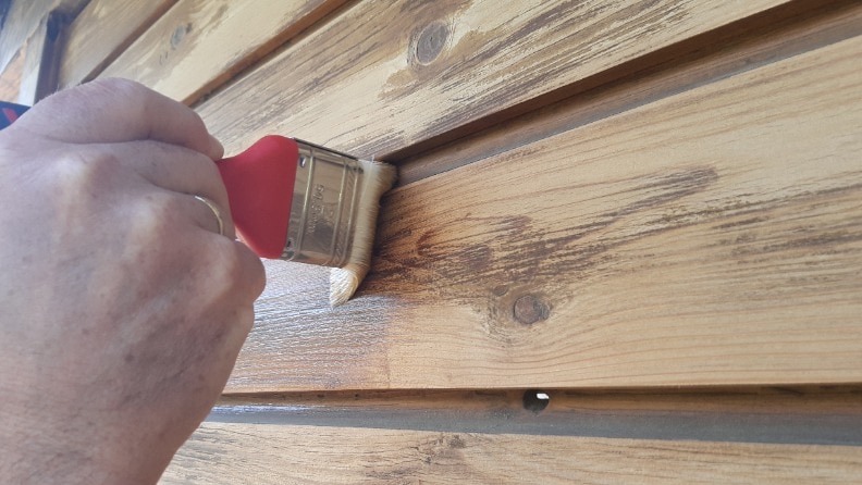Ein Mann trägt mit einem Pinsel Holzschutzlasur auf einen Carport auf