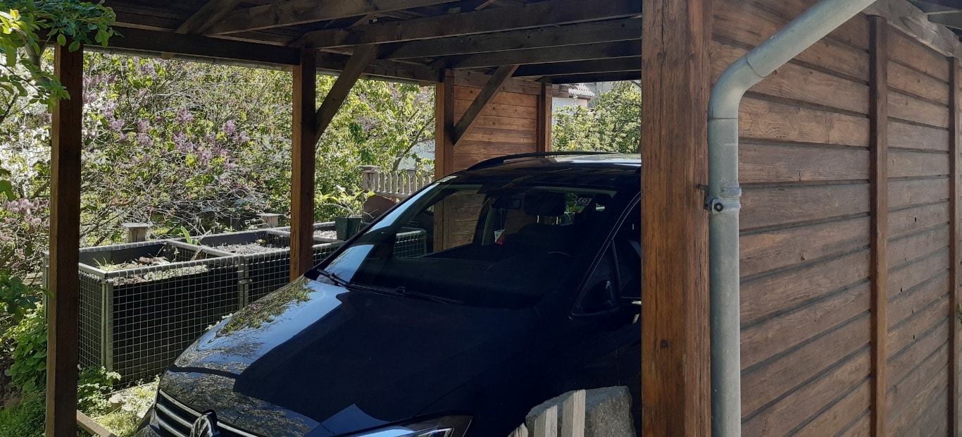 Ein mit einer Holzschutz-Lasur von Xyladecor neu gestrichener Carport mit einem Auto und angrenzendem Garten