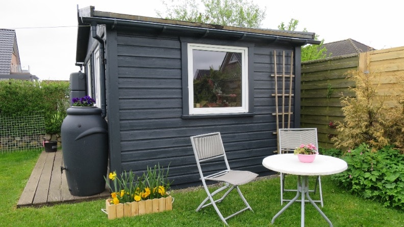 Anthrazitgraues Gartenhaus in einem gepflegten Garten mit Gartenmöbeln im Vordergrund