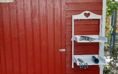 Gartenhaus gestrichen in Schwedenrot von Consolan mit einem weißen Regal für Gartenwerkzeuge