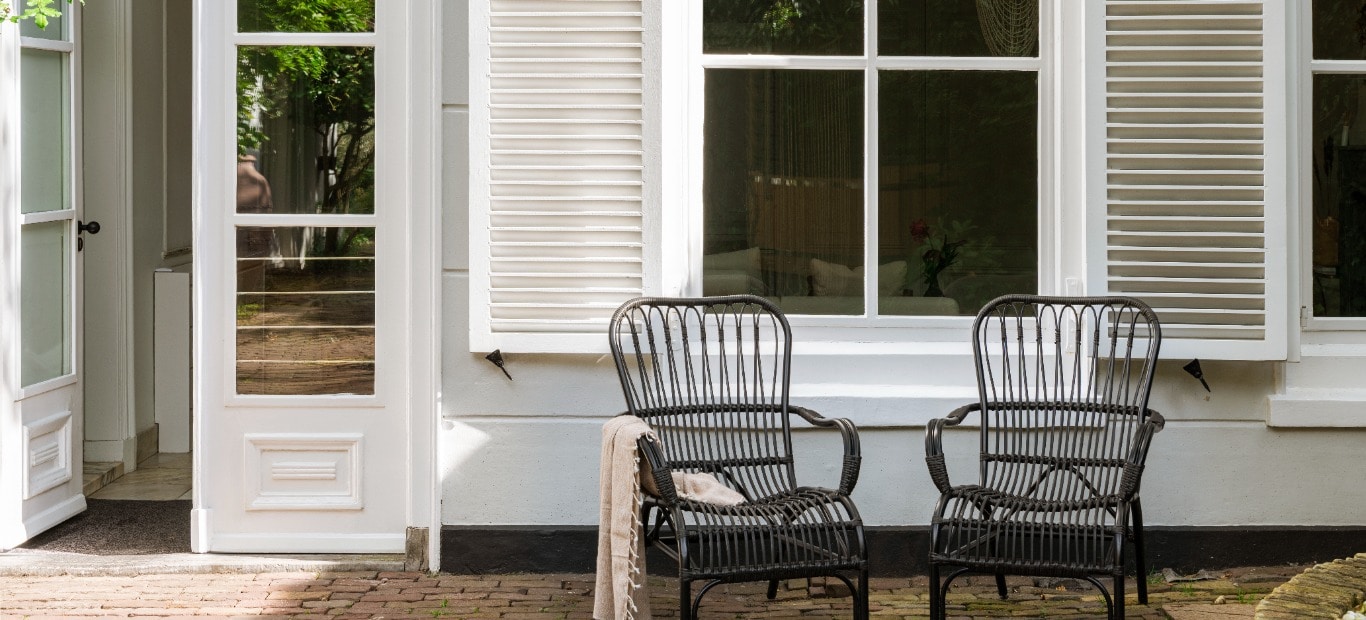 Mit Consolan gestrichene Fensterläden an einem Haus, davor zwei Korbstühle