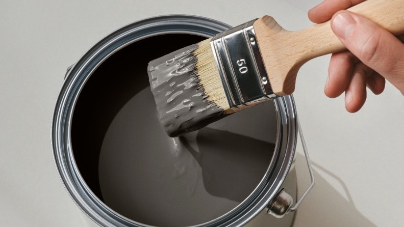 Ein Flachpinsel wird in eine Dose mit Wetterschutzfarbe von Consolan getaucht, um Fensterläden zu streichen