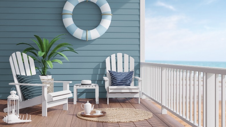 Terrasse eines Hauses am Meer mit einer in maritimem Blau gestrichenen Holzfassade, Sitzmöbeln und einem Schwimmring als Deko