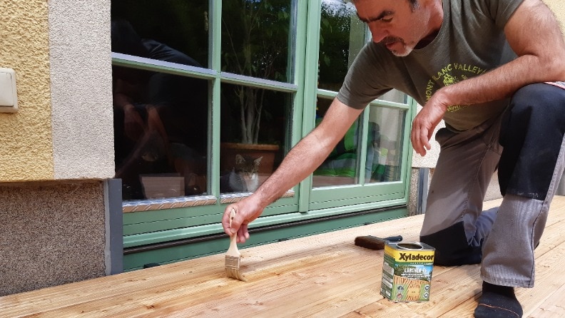 Ein Mann trägt mit einem Pinsel Lärchen-Öl von Xyladecor auf seiner neuen Holzterrasse auf